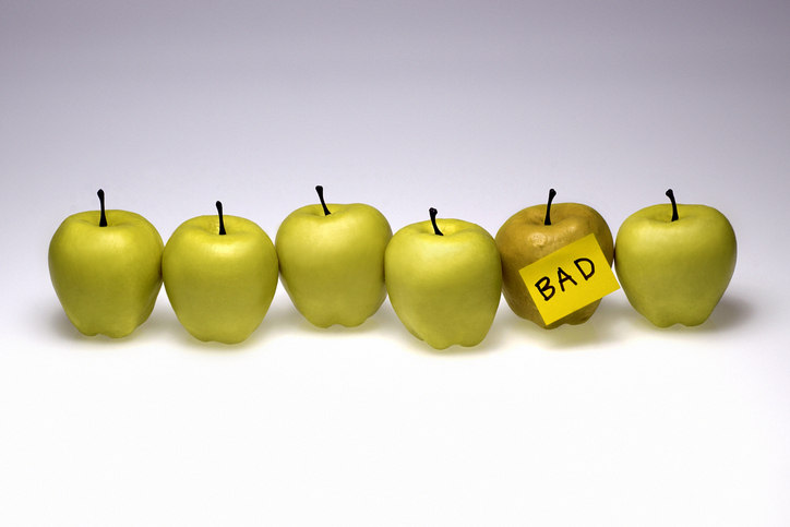 6 green apples in a line; 1 has a sticky note on it that says "bad"