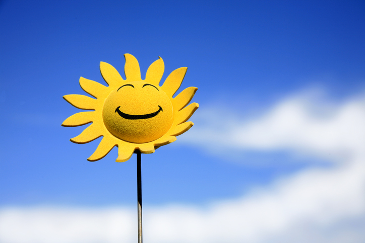 A drawing of a yellow sunflower with a smiling face with a blue sky in the background