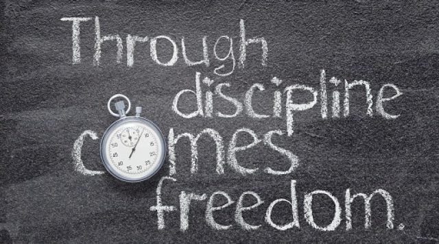 The words "through discipline comes freedom" written on a chalkboard. The "o" in the word "comes" is a round stopwatch.
