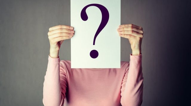photo of a person holding a large piece of paper with a question mark on it, covering their face