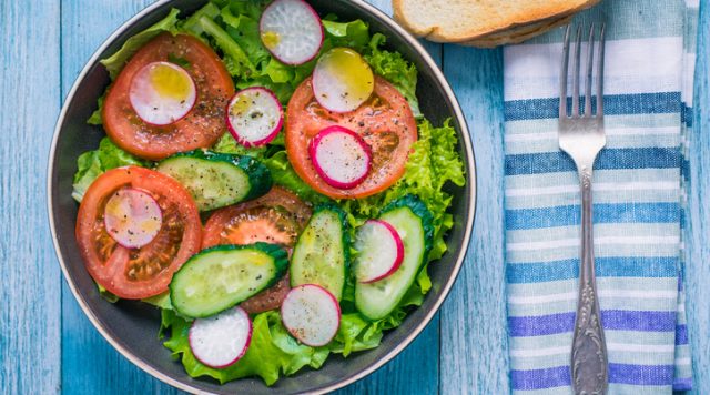 Healthy vegetarian salad with fresh tomatoes, cucumbers, onions, lettuce and radishes with olive oil on a rustic wooden background - top view