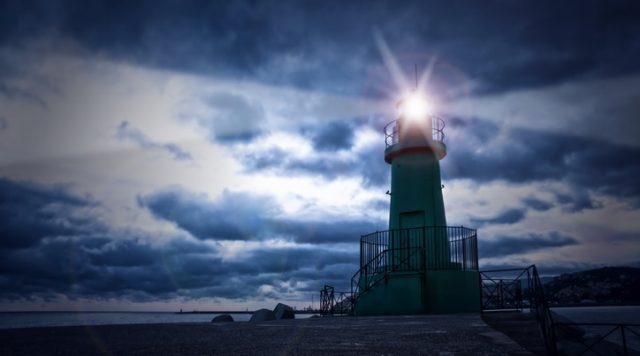 A lighthouse with a bright light shining through a cloudy sky