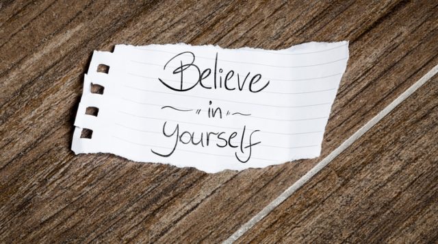A brown background with a white piece of paper that says "believe in yourself"