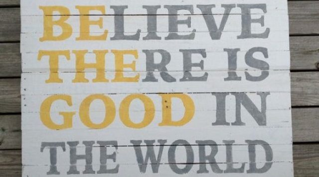 A sign that says "believe there is good in the world" in gray letters with "be the good" in yellow letters