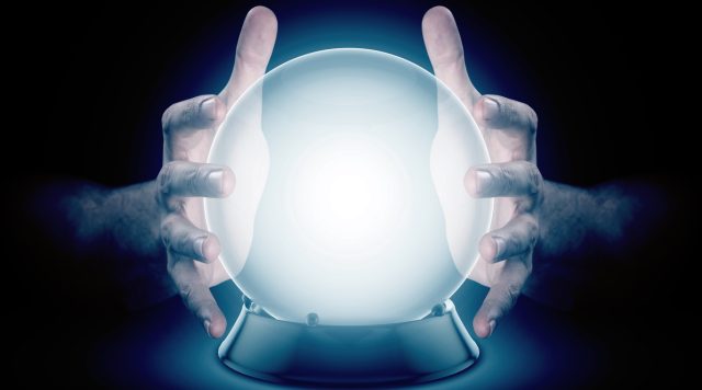 A pair of male hands surrounding a crystal ball conjuring up a hologram on an isolated dark studio background