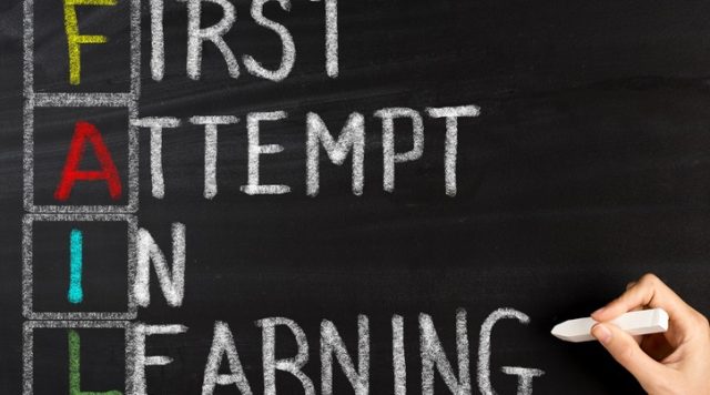 The words "first attempt in learning" written on a chalkboard in white chalk with the first letter of each word written in color and a box drawn around the letter. These letters spell out the word "fail"