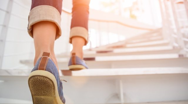 A person putting their right foot onto the first step of a staircase