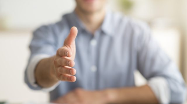 A smiling man with his hand outstretched for a handshake