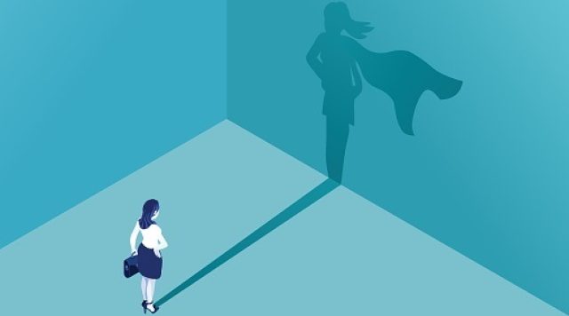 Illustration of a woman facing a wall looking at her shadow. Her shadow is her with a superhero cape on.