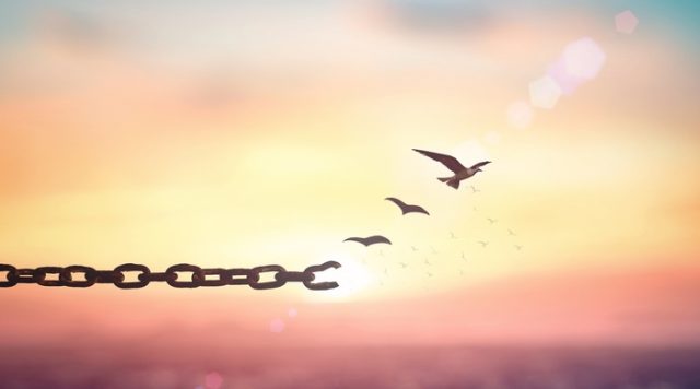 A sunny sky in the background with a chain in the foreground. The last chain link is broken and there are birds flying away from it.