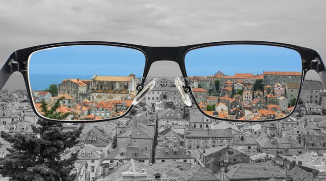 The view of a city through a pair of glasses with the background in gray and the view through the lenses of the glasses is in color
