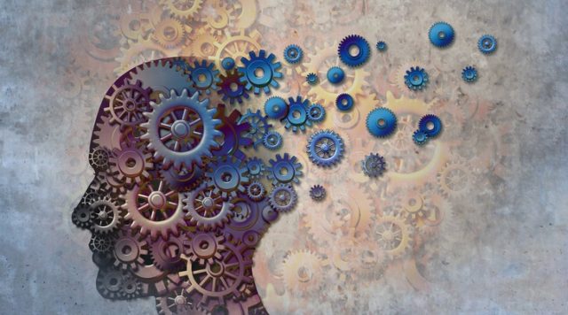 Silhouette of a human head in side profile, made up of gears, with some of the gears floating out from the back of the head