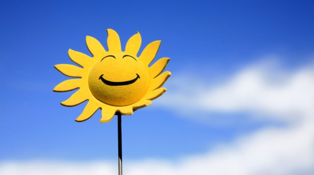 A drawing of a yellow sunflower with a smiling face with a blue sky in the background