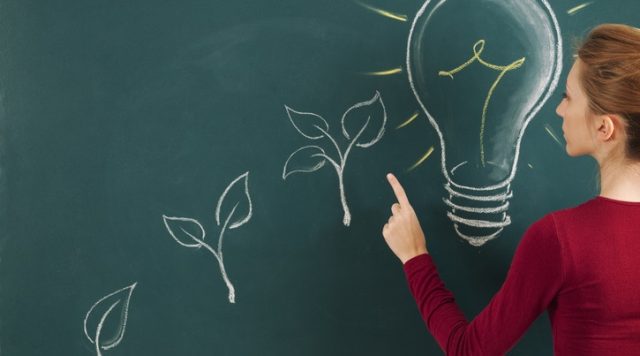 A person drawing at a chalkboard. The drawings are (from left to right, and in ascending order): a plant with 1 leaf, a plant with 2 leaves, a plant with 3 leavens, then finally a large light bulb